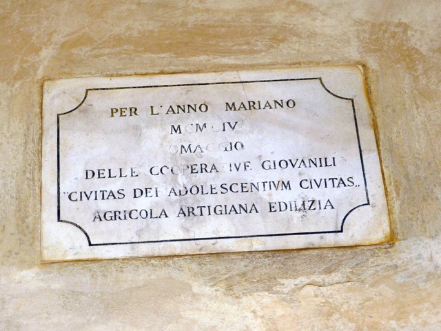 La targa ricorda il restauro di una parte dei portici di San Luca nel 1954 grazie all'offerta della Coop. Città dei Ragazzi